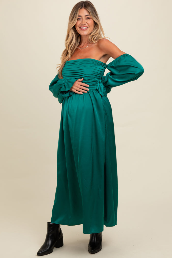 woman wearing a dark green off-the-shoulder maternity dress with puff sleeves, holding her baby bump