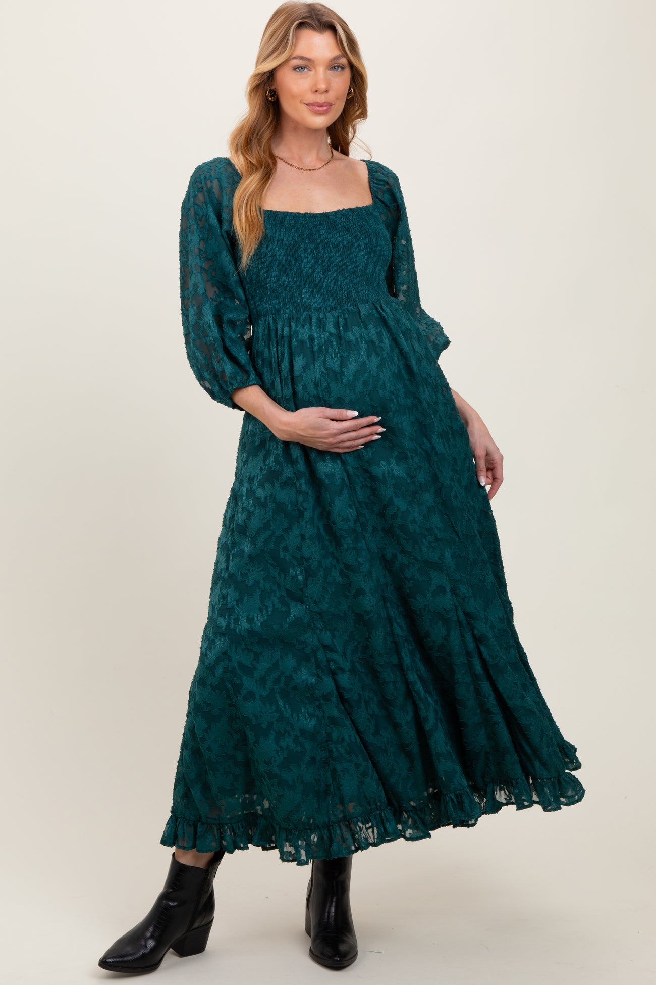 woman wearing a teal puff sleeve maternity dress with smocked bodice and a flowing skirt, showing her baby bump