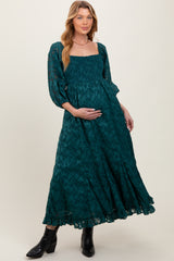 woman wearing a teal puff sleeve maternity dress with smocked bodice and a flowing skirt, showing her baby bump