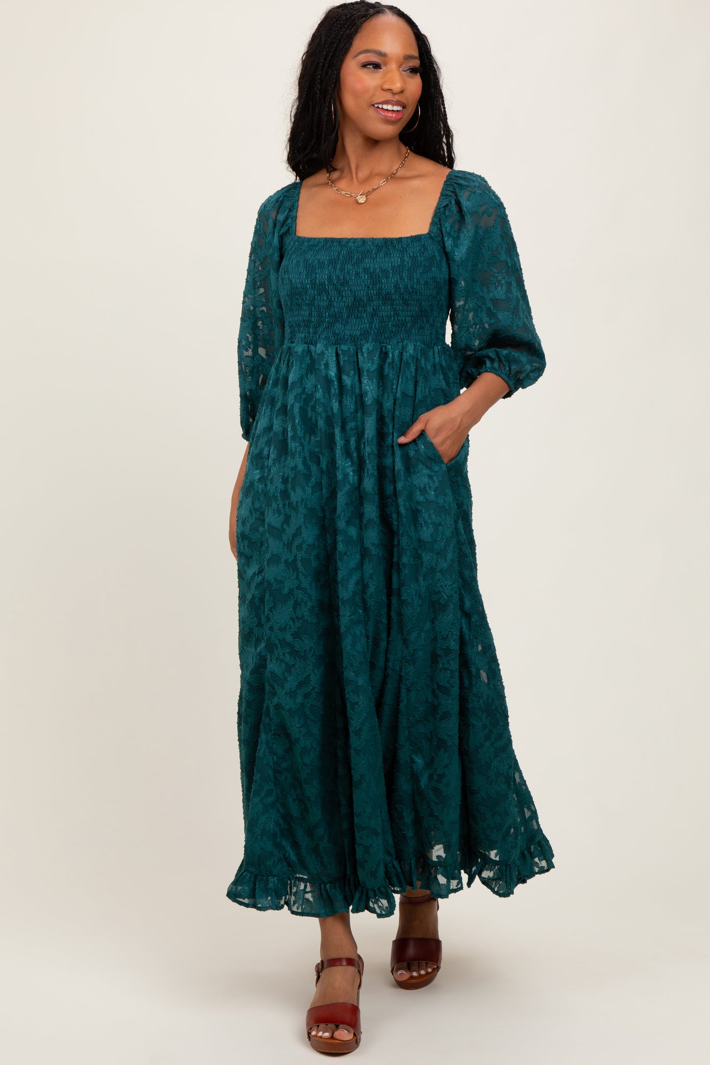 woman wearing a teal long sleeve maxi dress with a square neckline and pockets, styled with brown ankle strap heels