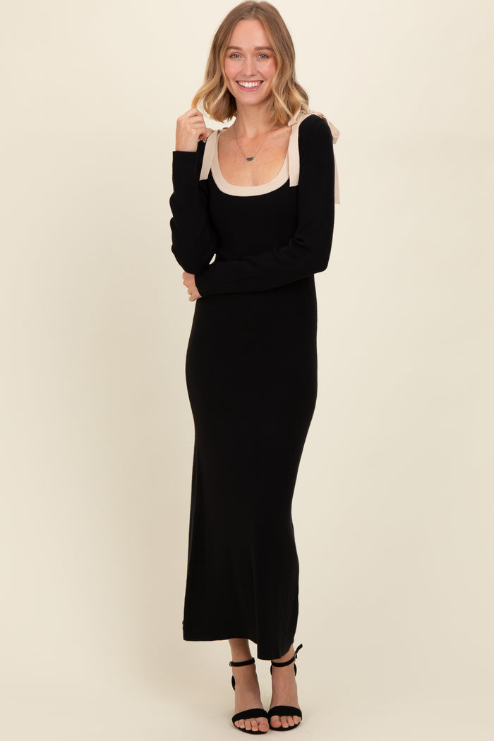 woman wearing a black long sleeve maxi dress with a nude scoop neckline and bow shoulder details, smiling at the camera