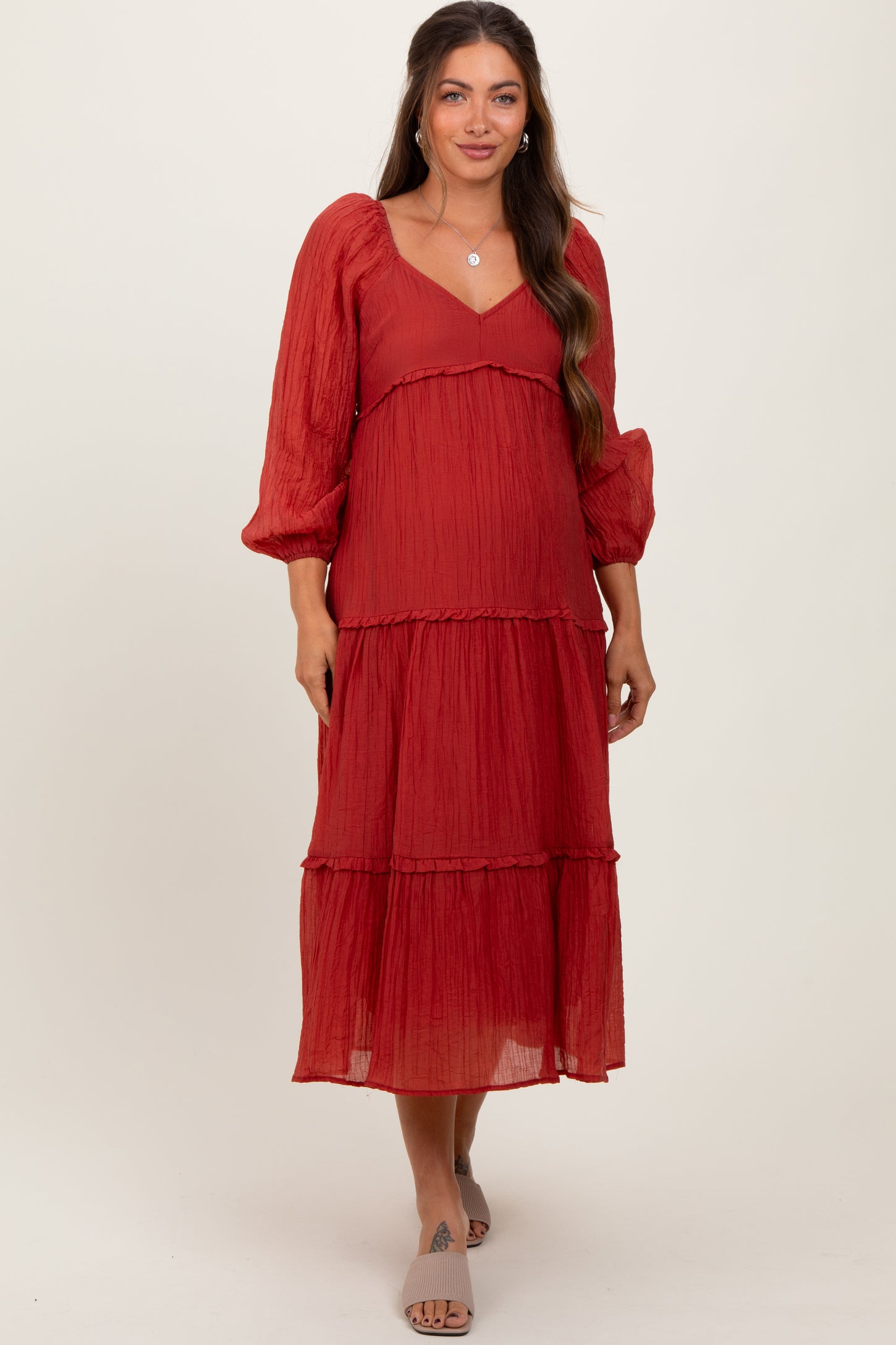 woman wearing a rust red tiered maternity dress with balloon sleeves and a v-neckline, showcasing her baby bump