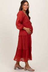 woman wearing a red tiered maternity maxi dress, cradling her baby bump, with long sleeves and a v-neckline