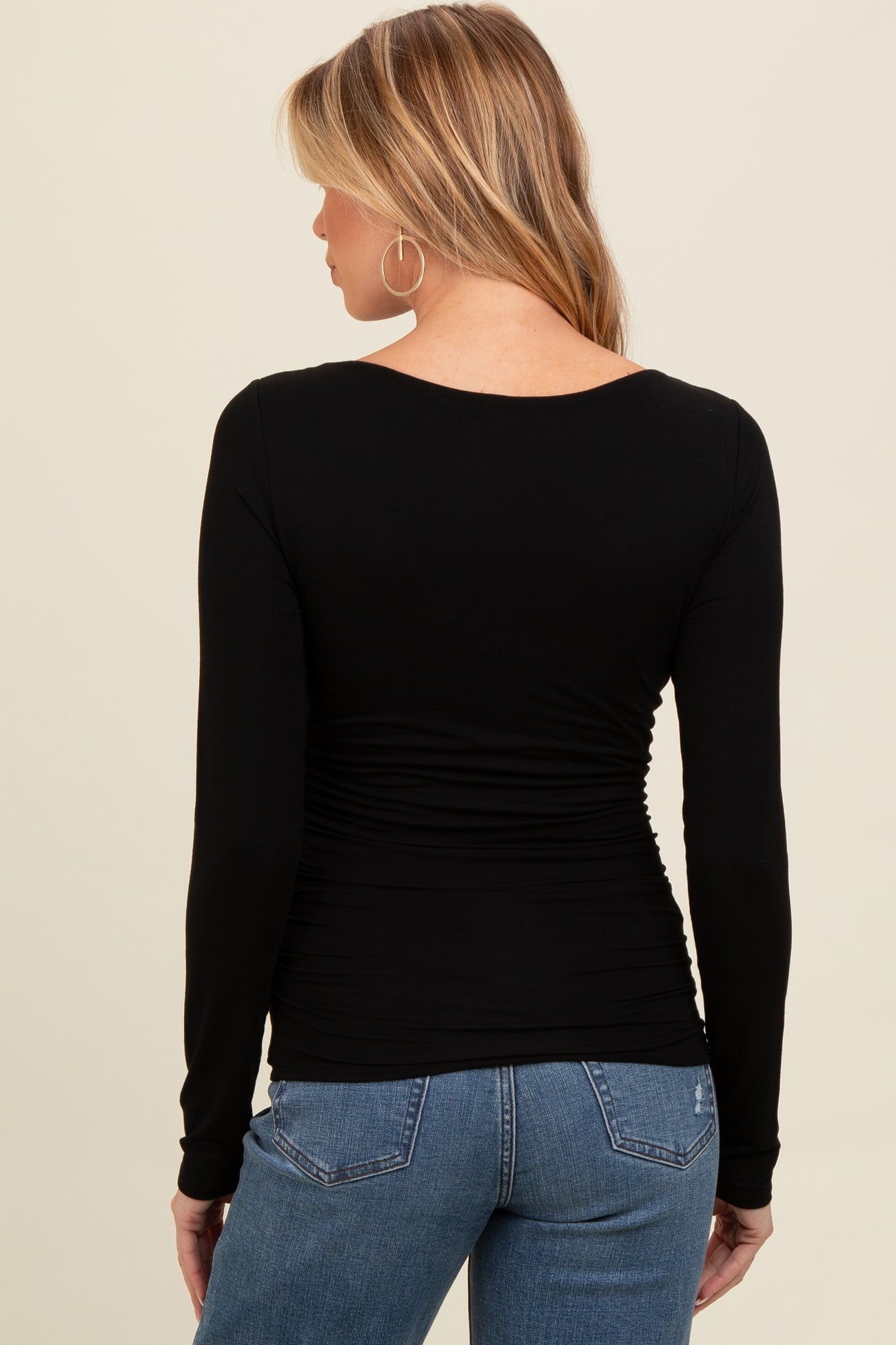 woman wearing a black long sleeve maternity top with gathered details at the waist and blue jeans