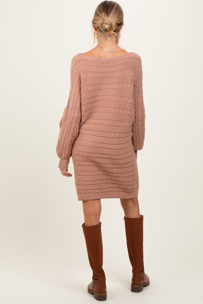 woman wearing a taupe cable knit maternity sweater dress and knee-high brown boots, showing off her baby bump from the back