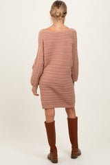 woman wearing a taupe cable knit maternity sweater dress and knee-high brown boots, showing off her baby bump from the back
