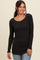 woman wearing a black long sleeve ribbed top with a scoop neckline and scalloped hem, smiling at the camera