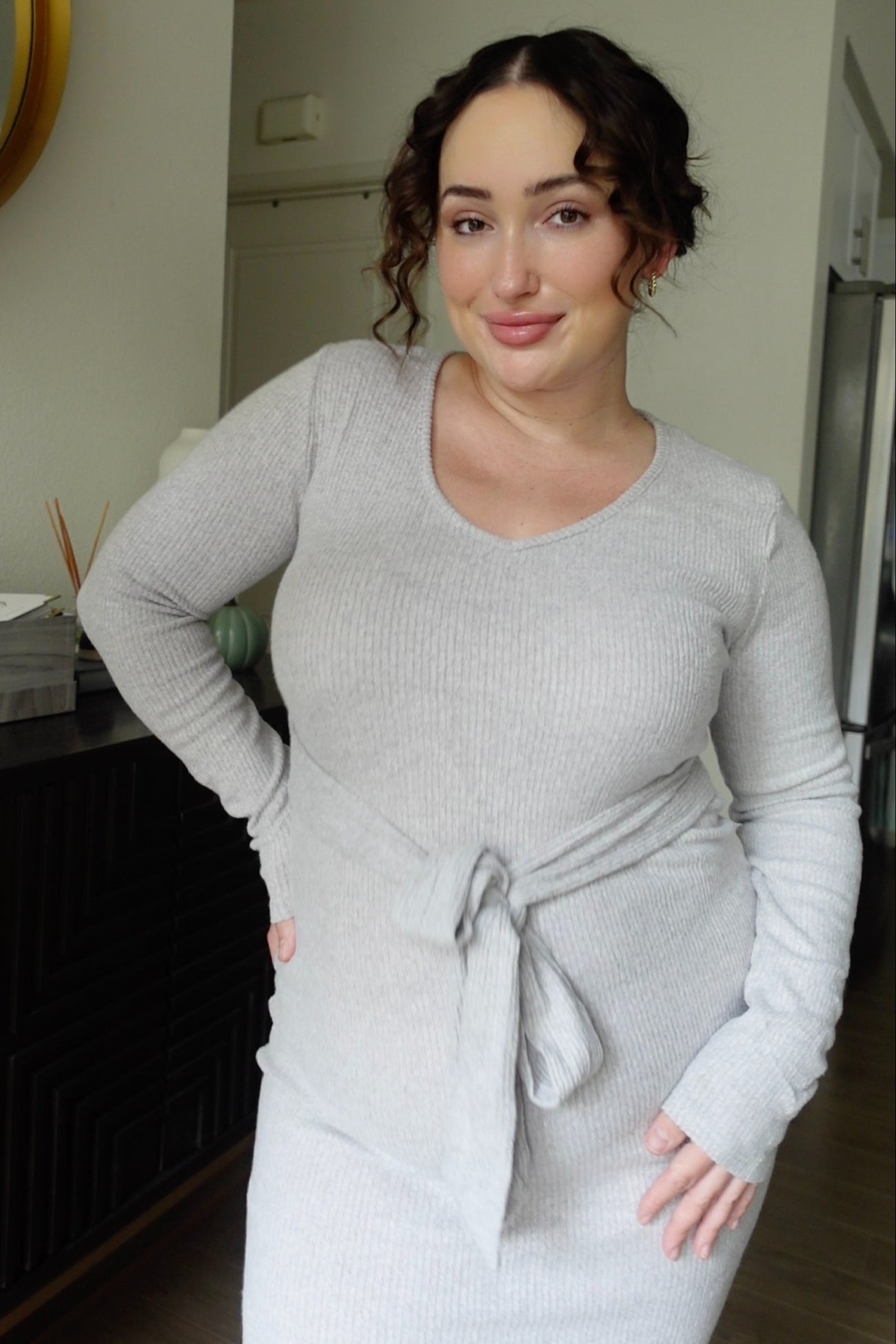 woman wearing a light grey ribbed maternity dress with a tie detail at the waist and long sleeves, showing her baby bump