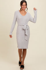 woman wearing a light gray ribbed sweater dress with a belted waist and long sleeves, posing confidently