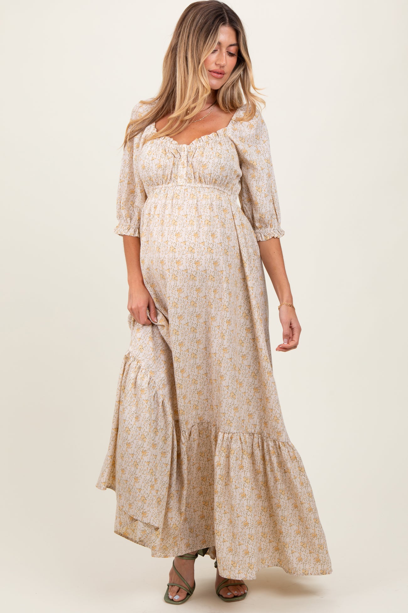 woman wearing a cream floral maternity maxi dress with puff sleeves and a tiered skirt, featuring a visible baby bump