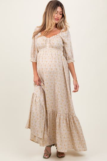 woman wearing a cream floral maternity maxi dress with puff sleeves and a tiered skirt, featuring a visible baby bump