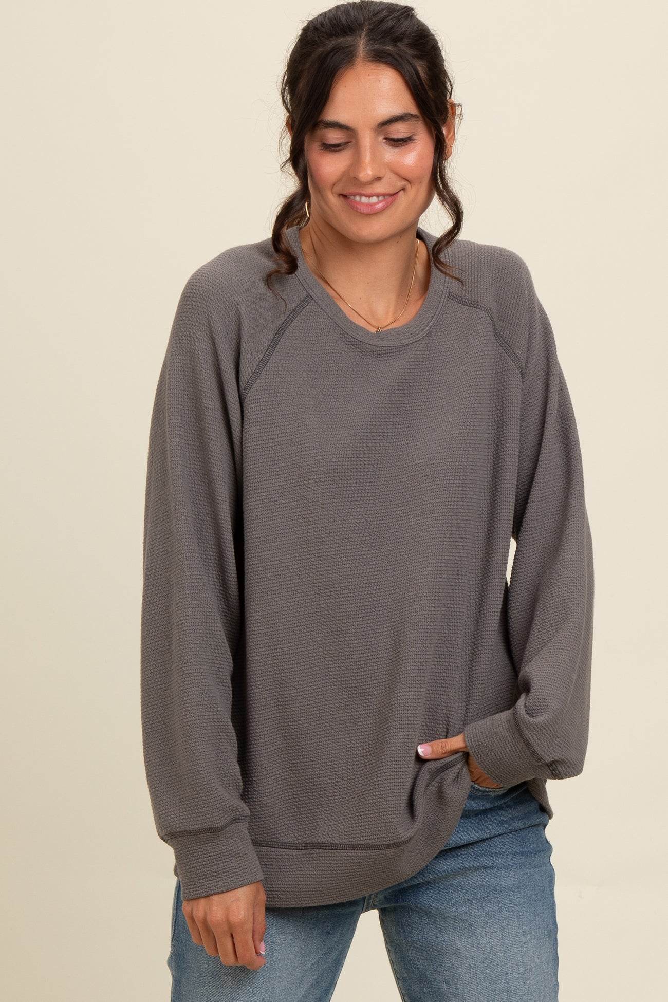 woman wearing a gray long sleeve sweatshirt with a relaxed fit and side pockets, styled with blue jeans