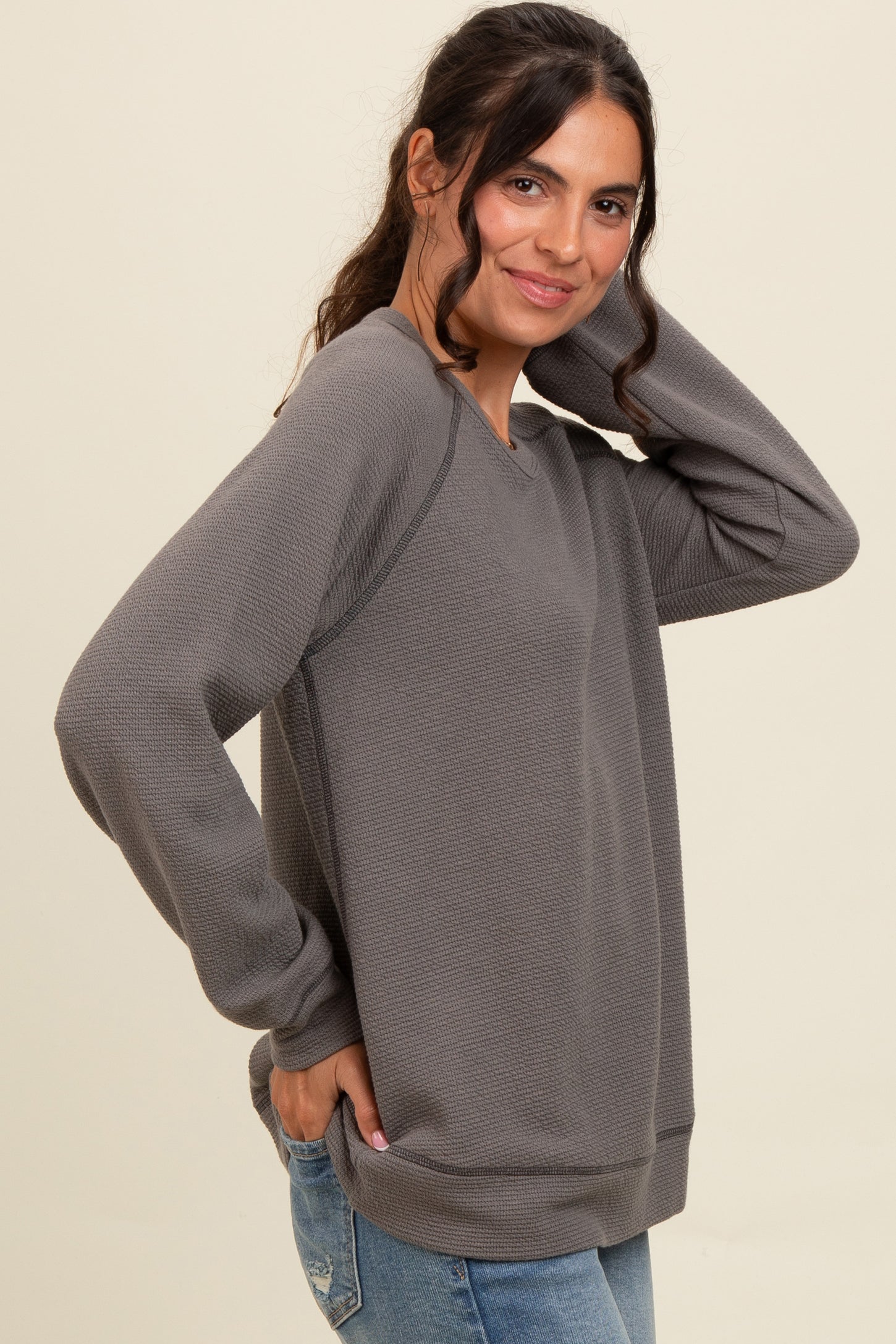 woman wearing a gray long sleeve sweatshirt with textured fabric and relaxed fit, posing with hand on her hair