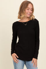 woman wearing a black long sleeve ribbed top and blue jeans, smiling while posing.