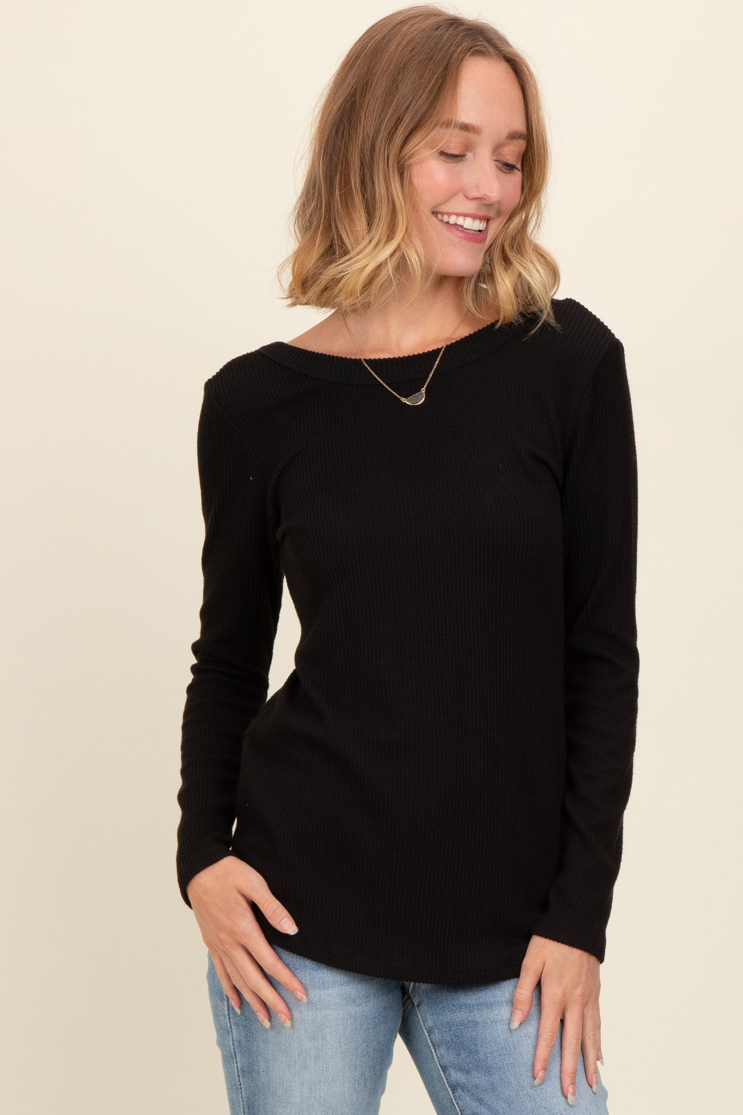 woman wearing a black long sleeve ribbed top and blue jeans, smiling while posing.