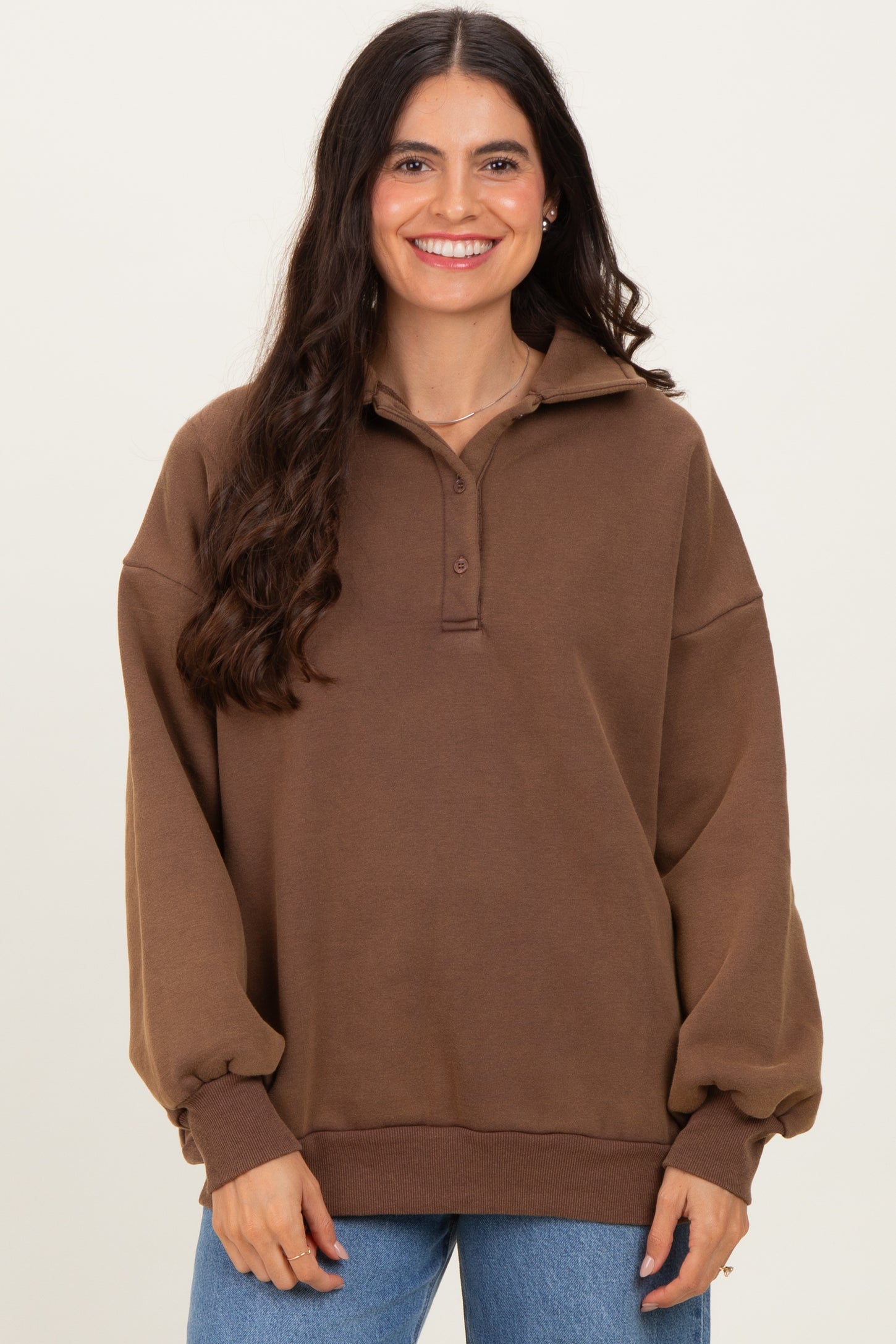 woman wearing a brown oversized pullover with a collar and button detailing, smiling at the camera