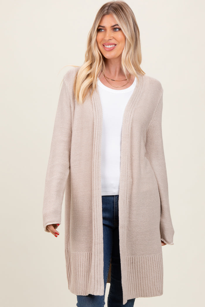 woman wearing a beige long cardigan over a white top and blue jeans, smiling at the camera