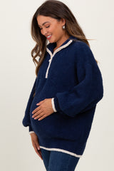 woman wearing a navy blue fleece maternity pullover with a white trim and holding her baby bump