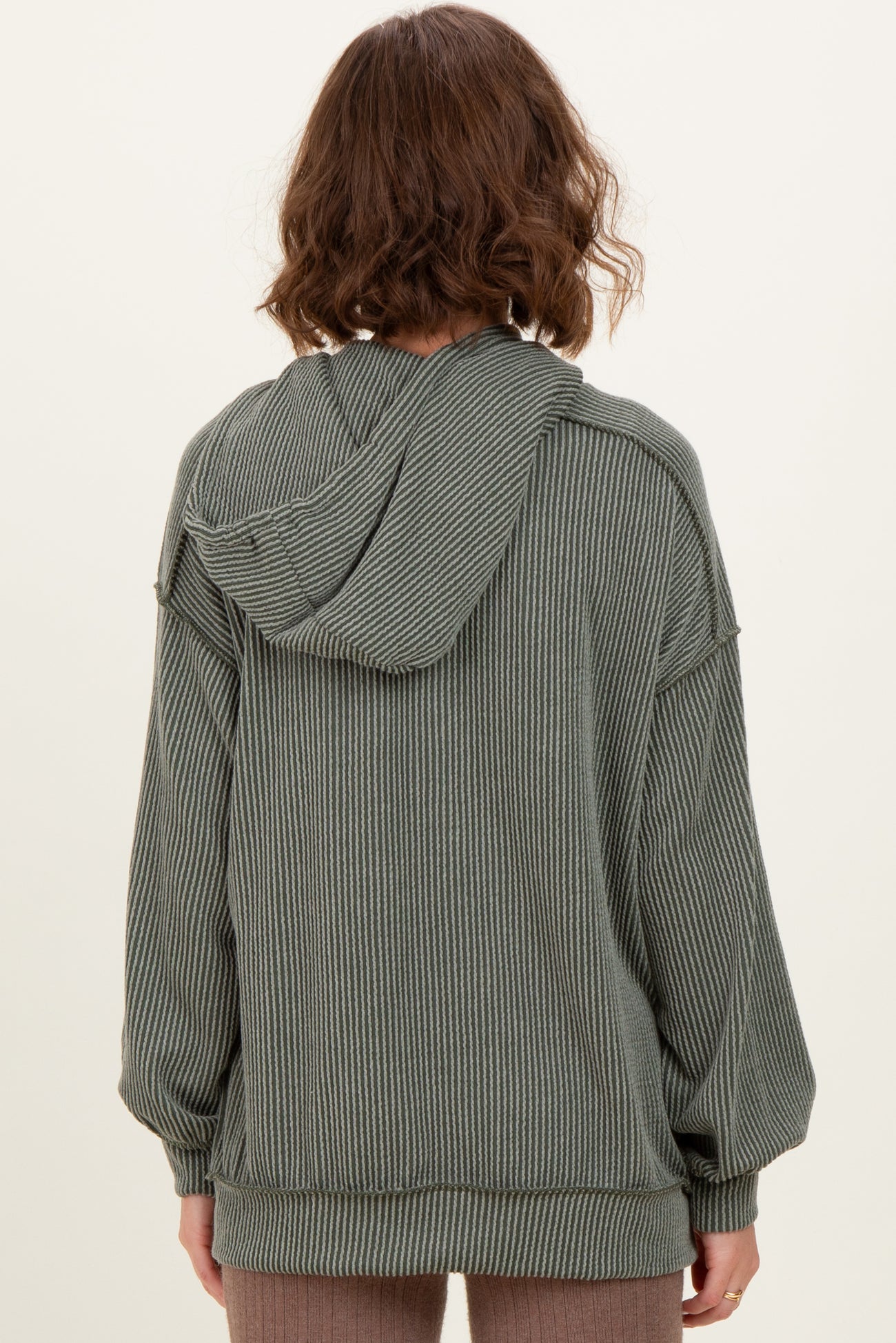woman wearing a green striped oversized hoodie with a hood and long sleeves, seen from the back