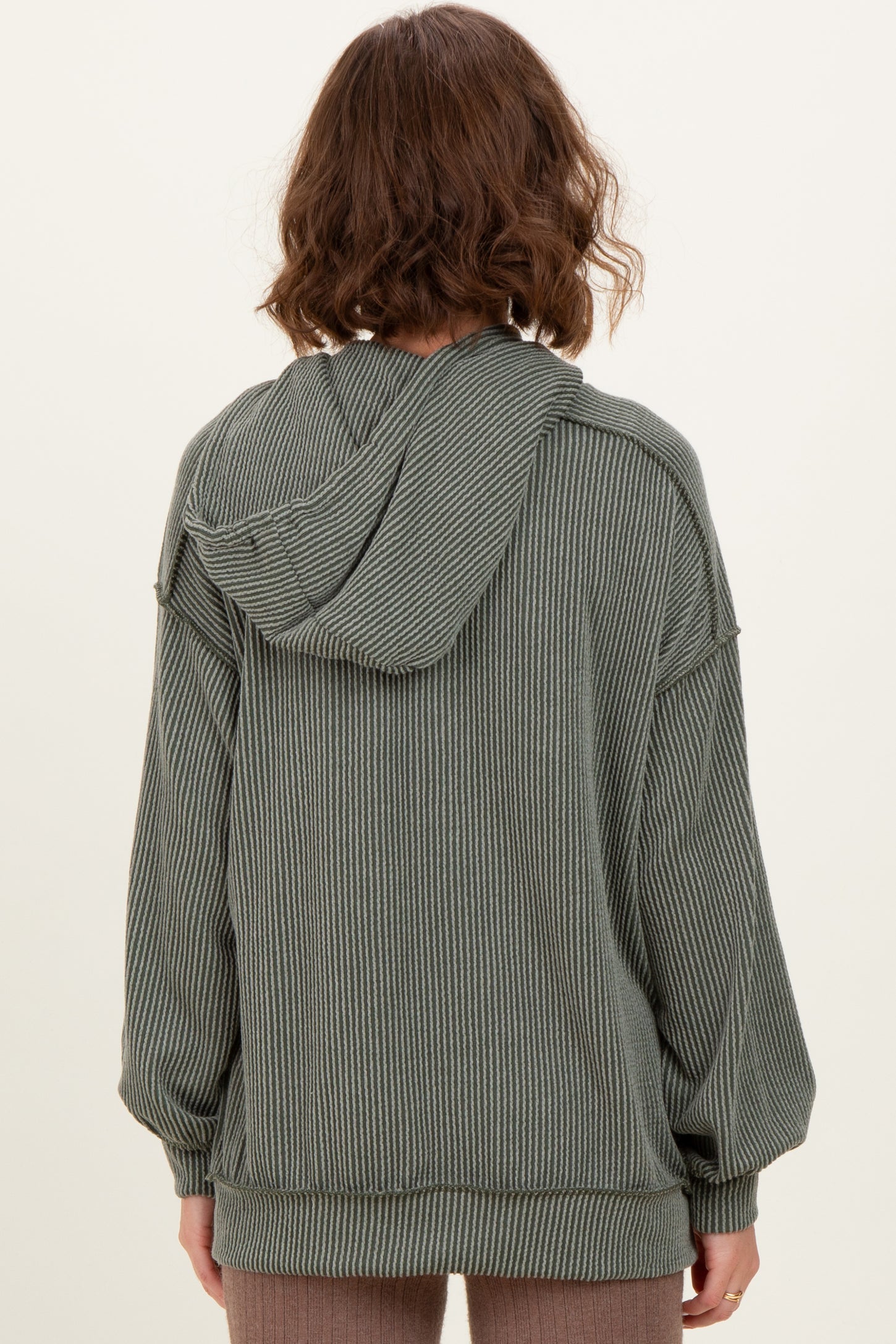 woman wearing a green striped oversized hoodie with a hood and long sleeves, seen from the back