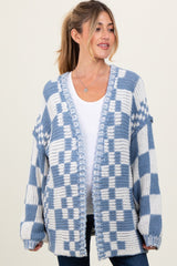 woman wearing a blue and white checkered maternity cardigan over a white top, with her hair styled in a ponytail