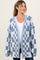 woman wearing a blue and white checkered maternity cardigan over a white top, with her hair styled in a ponytail