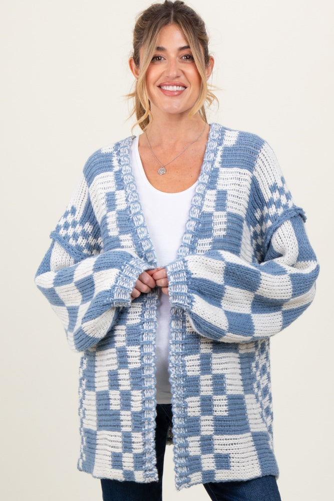 woman wearing a blue and white checkered maternity cardigan over a white top, smiling at the camera