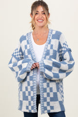 woman wearing a blue and white checkered maternity cardigan over a white top, smiling at the camera