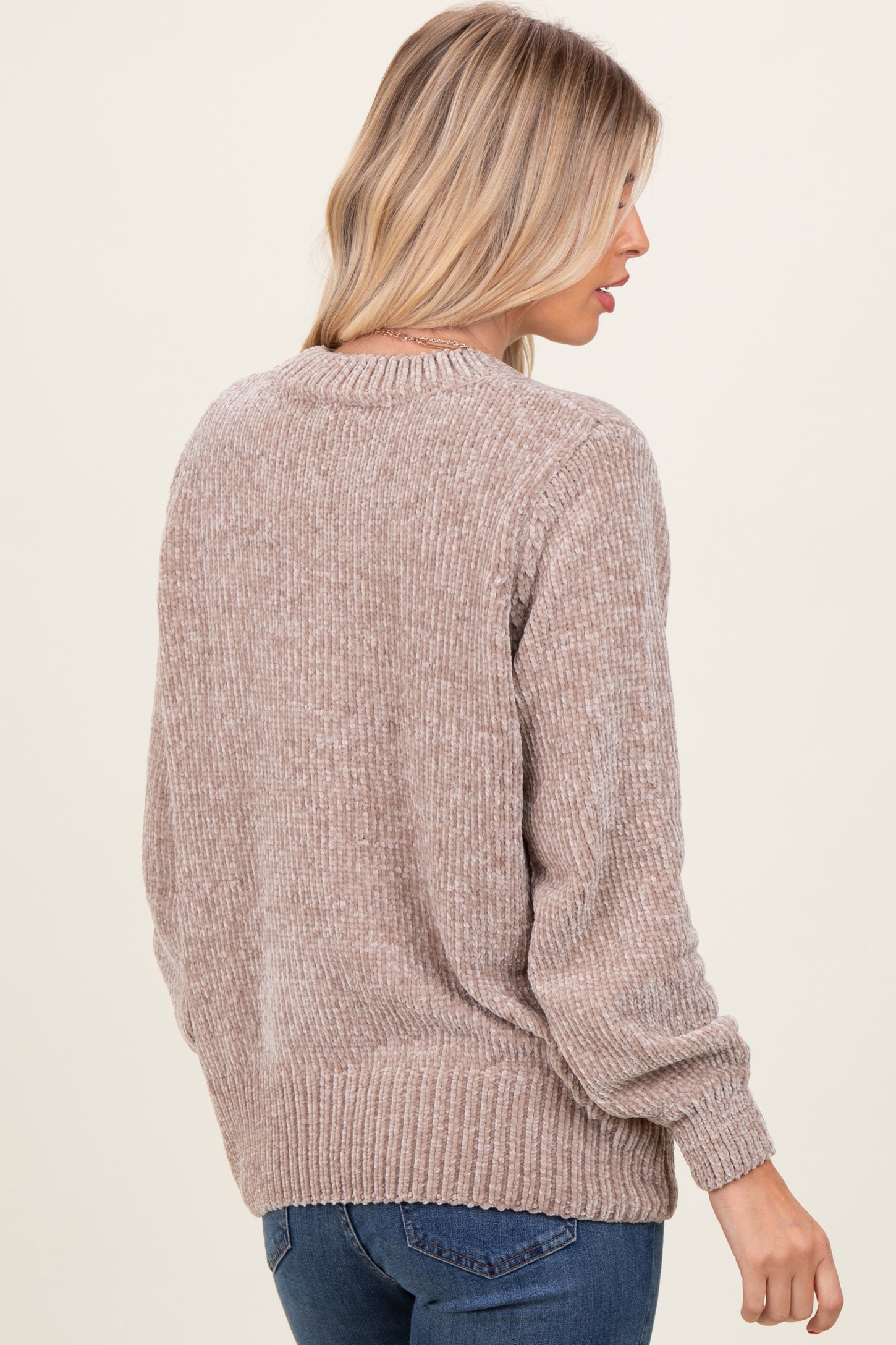 woman wearing a beige long sleeve knit sweater with a textured finish and ribbed hem, shown from the back