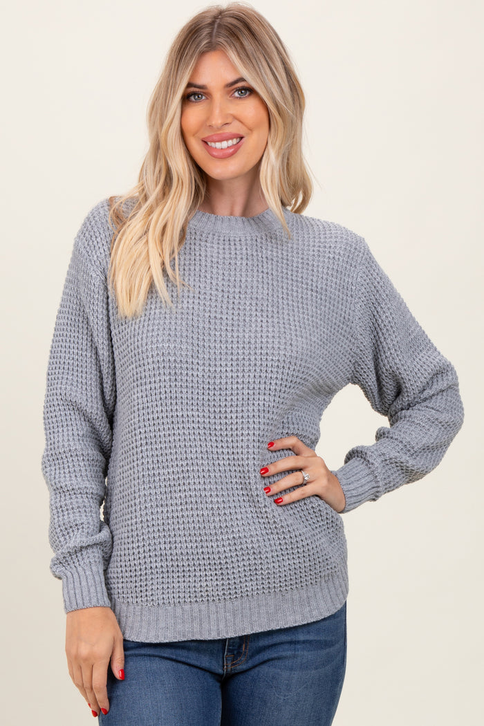 woman wearing a light gray knit sweater with a round neckline and relaxed fit, smiling with hands on her hips