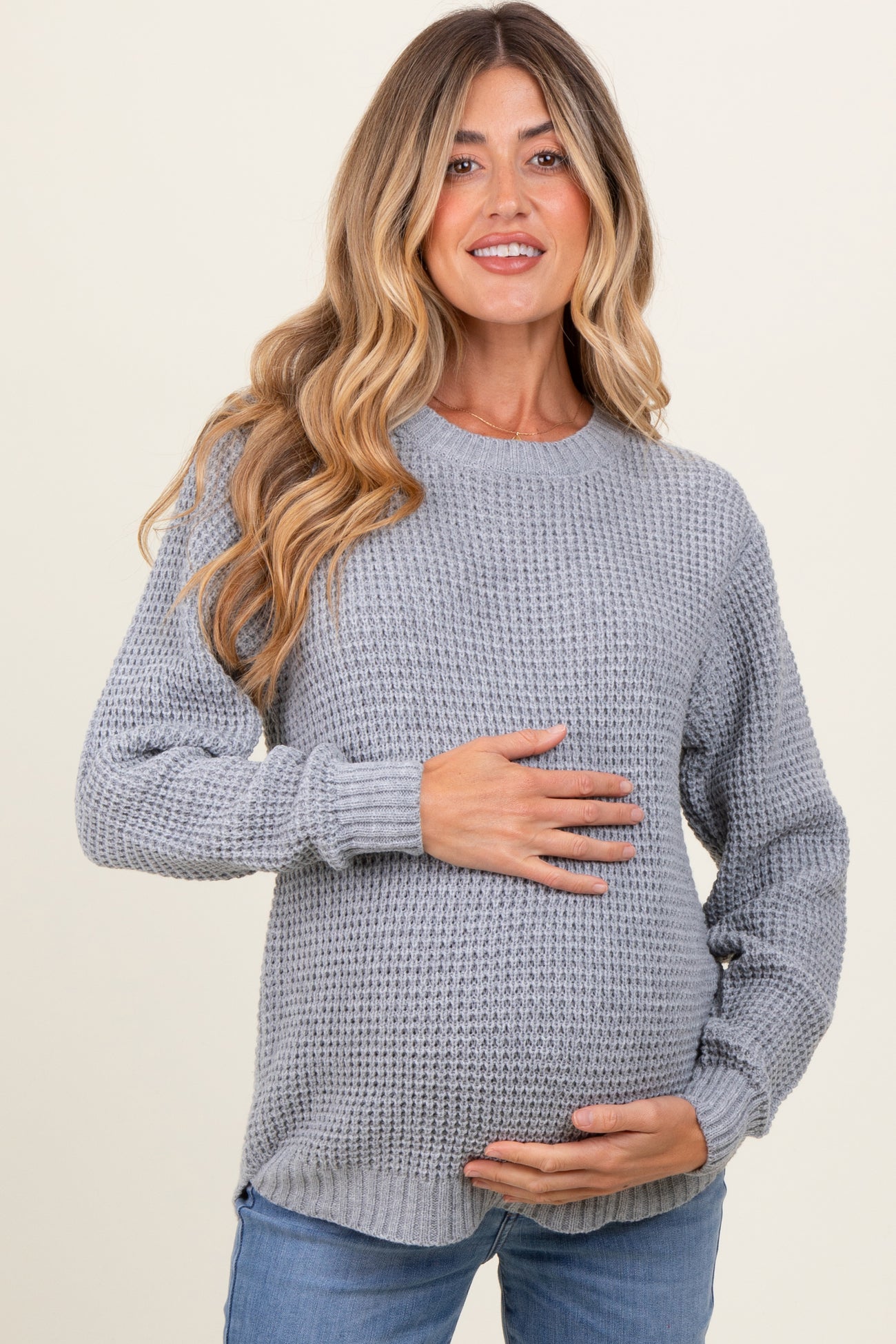 woman wearing a grey knitted maternity sweater and holding her baby bump