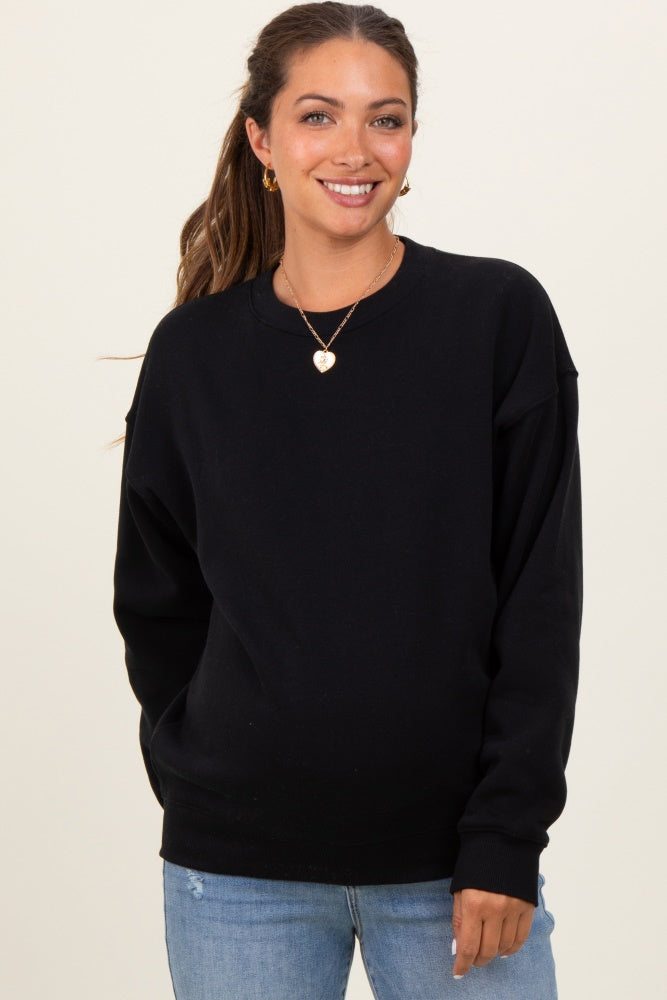 woman wearing a black oversized maternity sweatshirt and light blue jeans, smiling at the camera