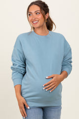 woman wearing a light blue maternity sweatshirt and holding her baby bump