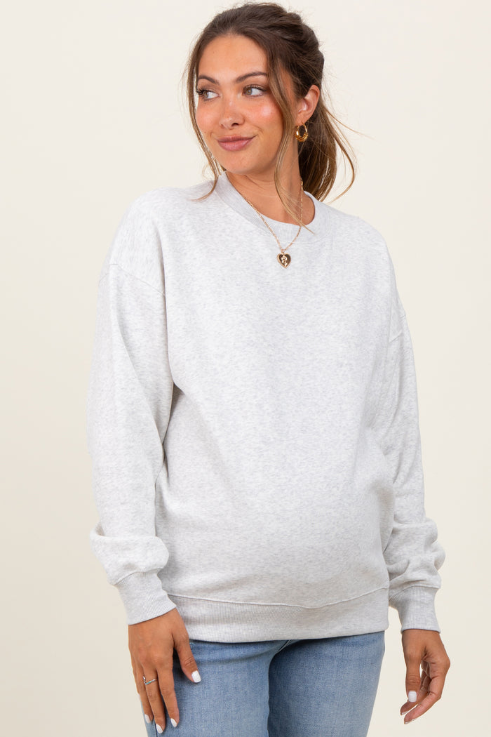 woman wearing a light grey oversized maternity sweatshirt and blue jeans with a visible baby bump