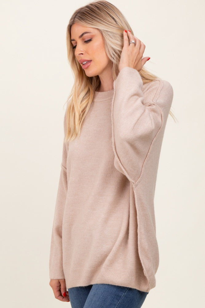 woman wearing a beige oversized sweater with side slits and long sleeves, styled with denim jeans
