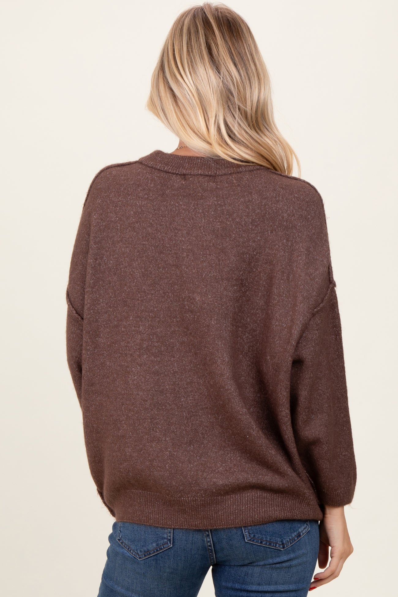 woman wearing a brown oversized sweater with a relaxed fit, seen from the back, paired with blue jeans