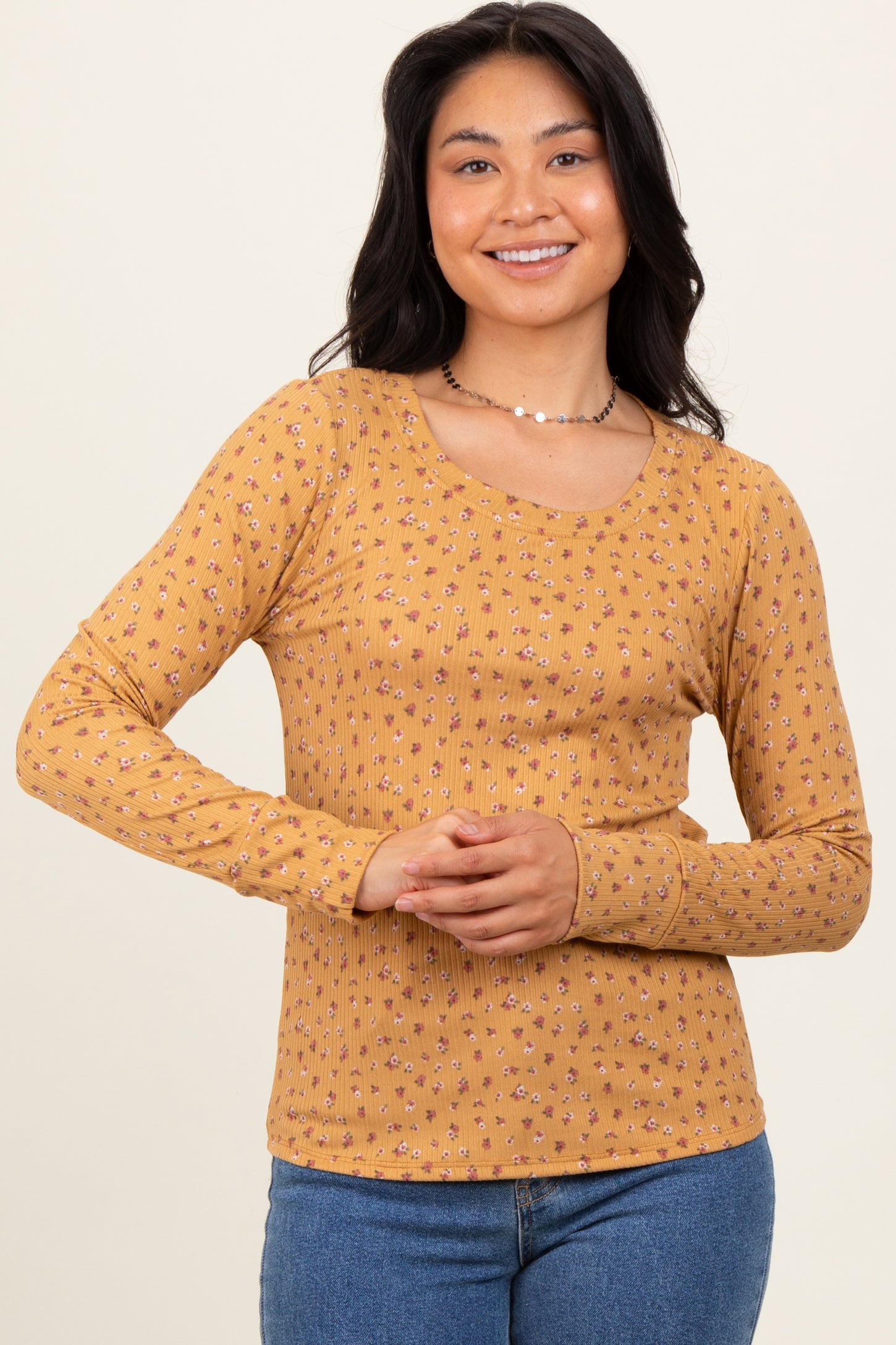 woman wearing a mustard long sleeve top with floral print and a scoop neckline, posing with hands clasped together