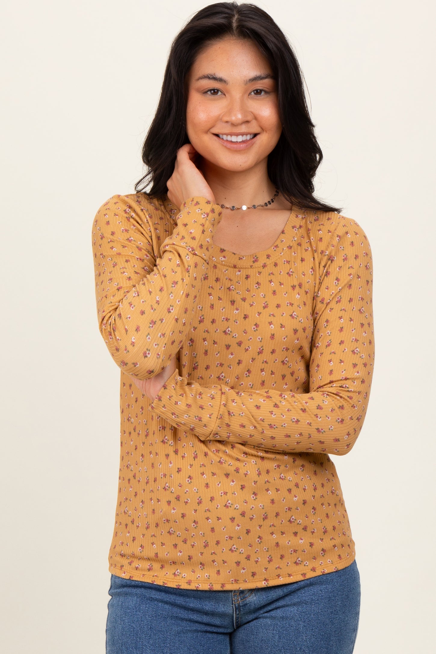 woman wearing a mustard long sleeve top with a floral pattern and scoop neckline, smiling at the camera