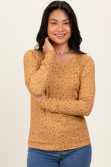 woman wearing a mustard long sleeve top with a floral pattern and scoop neckline, smiling at the camera