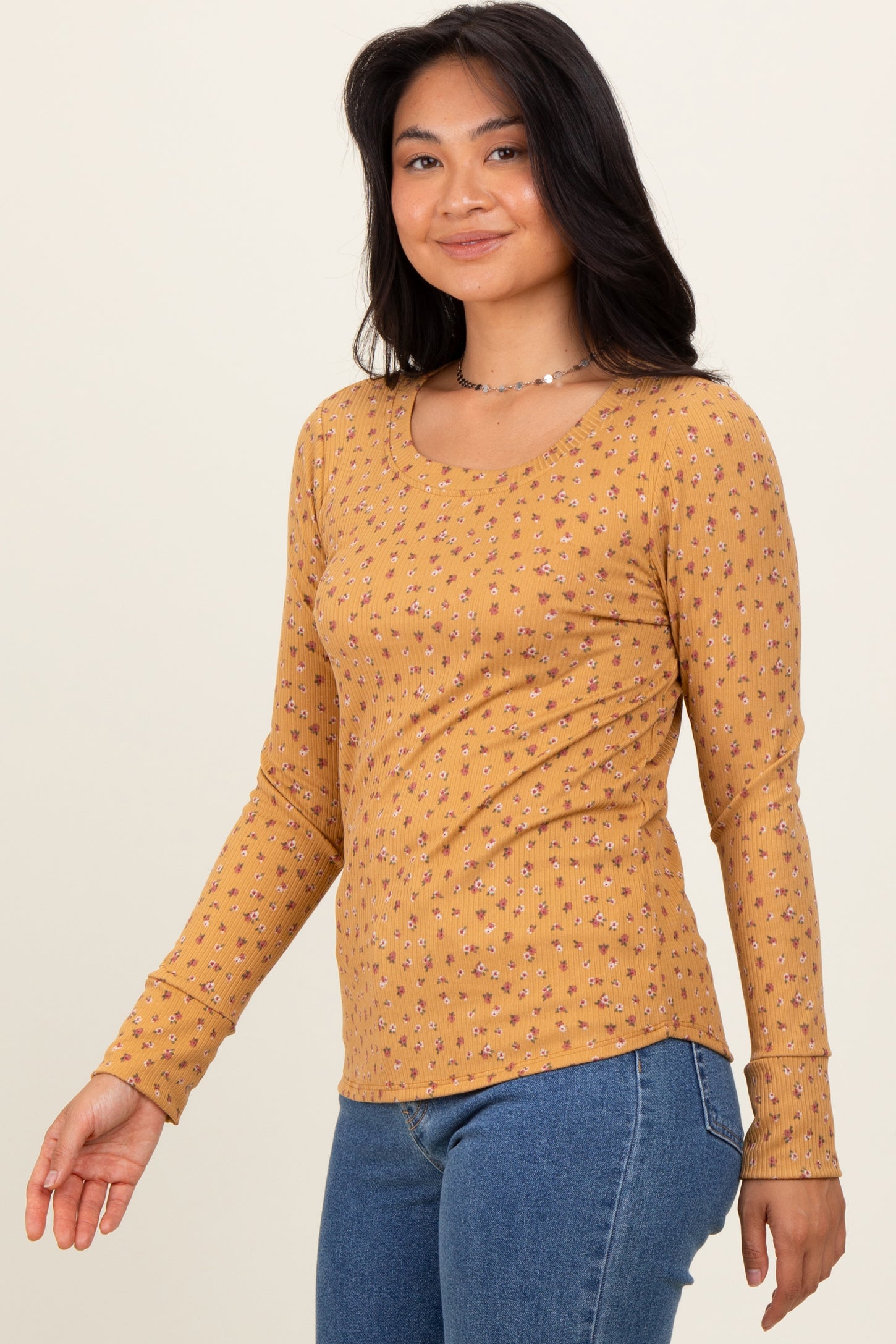 woman wearing a mustard yellow long sleeve top with tiny floral patterns and a scoop neckline, paired with blue jeans