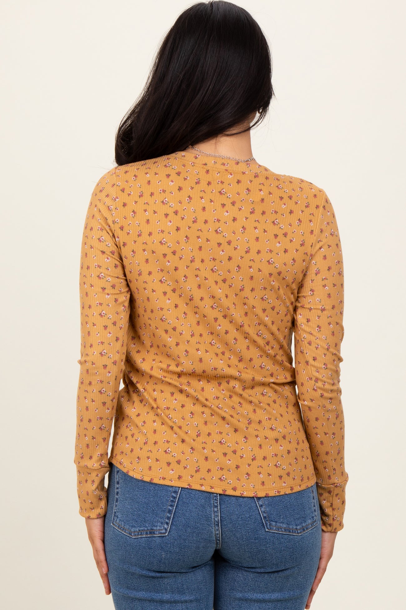 woman wearing a mustard long sleeve top with a floral print, viewed from the back, paired with blue denim jeans