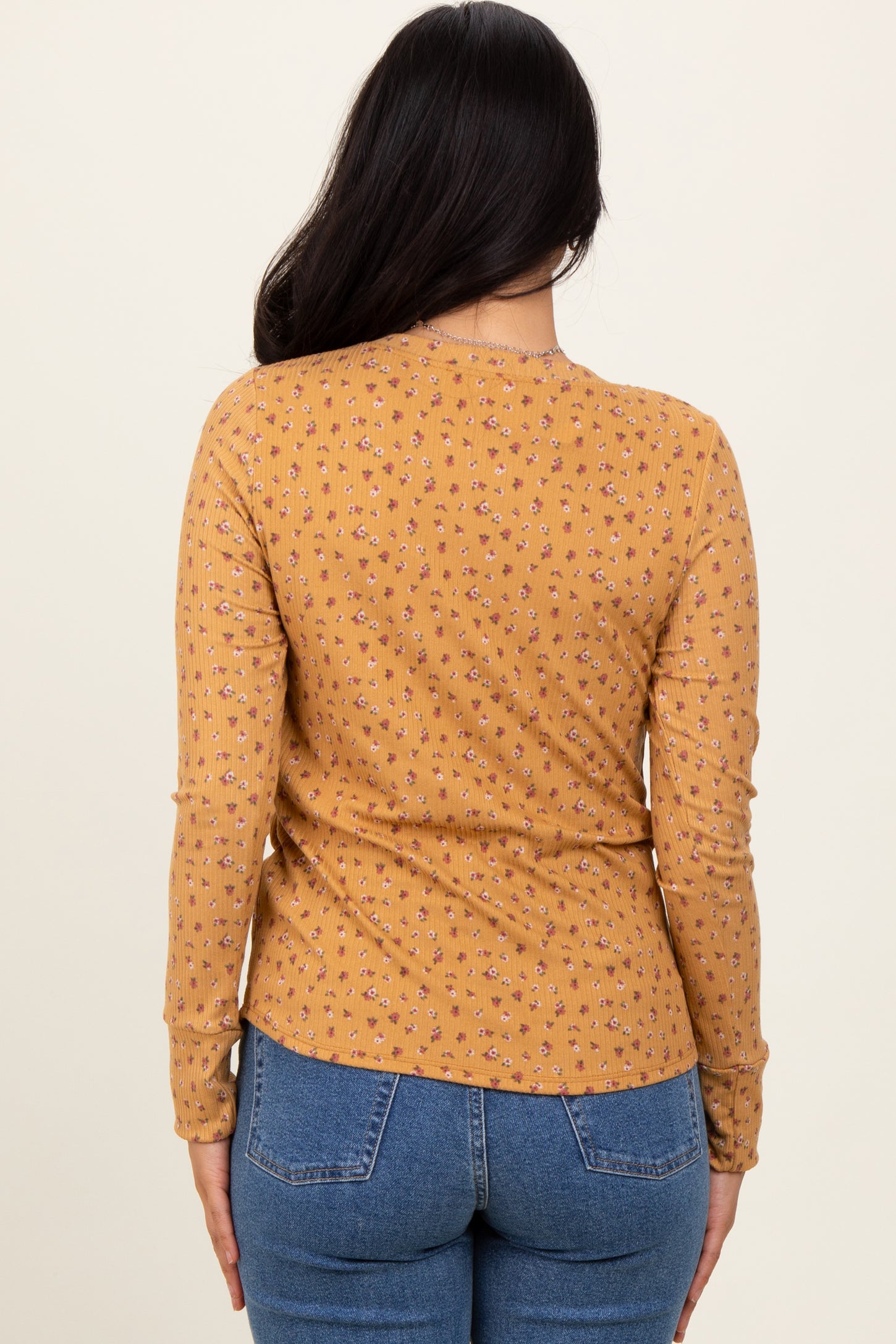 woman wearing a mustard long sleeve top with a floral print, viewed from the back, paired with blue denim jeans