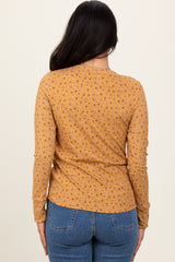 woman wearing a mustard long sleeve top with a floral print, viewed from the back, paired with blue denim jeans