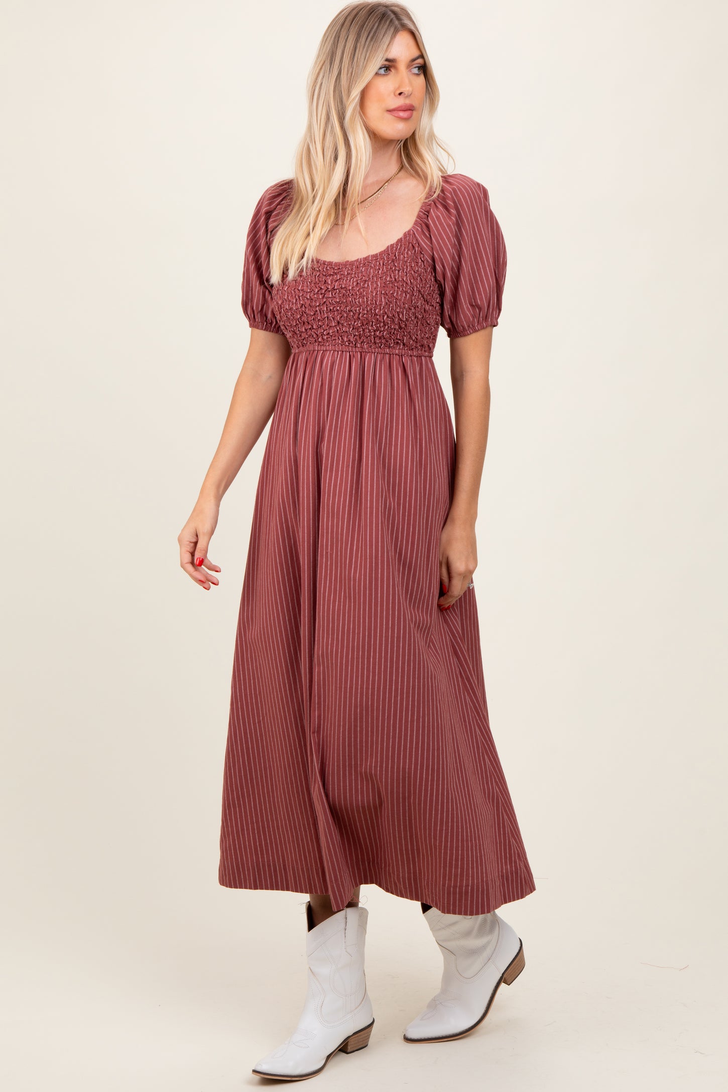woman wearing a rust-colored striped maxi dress with puff sleeves and a smocked bodice, paired with white cowboy boots
