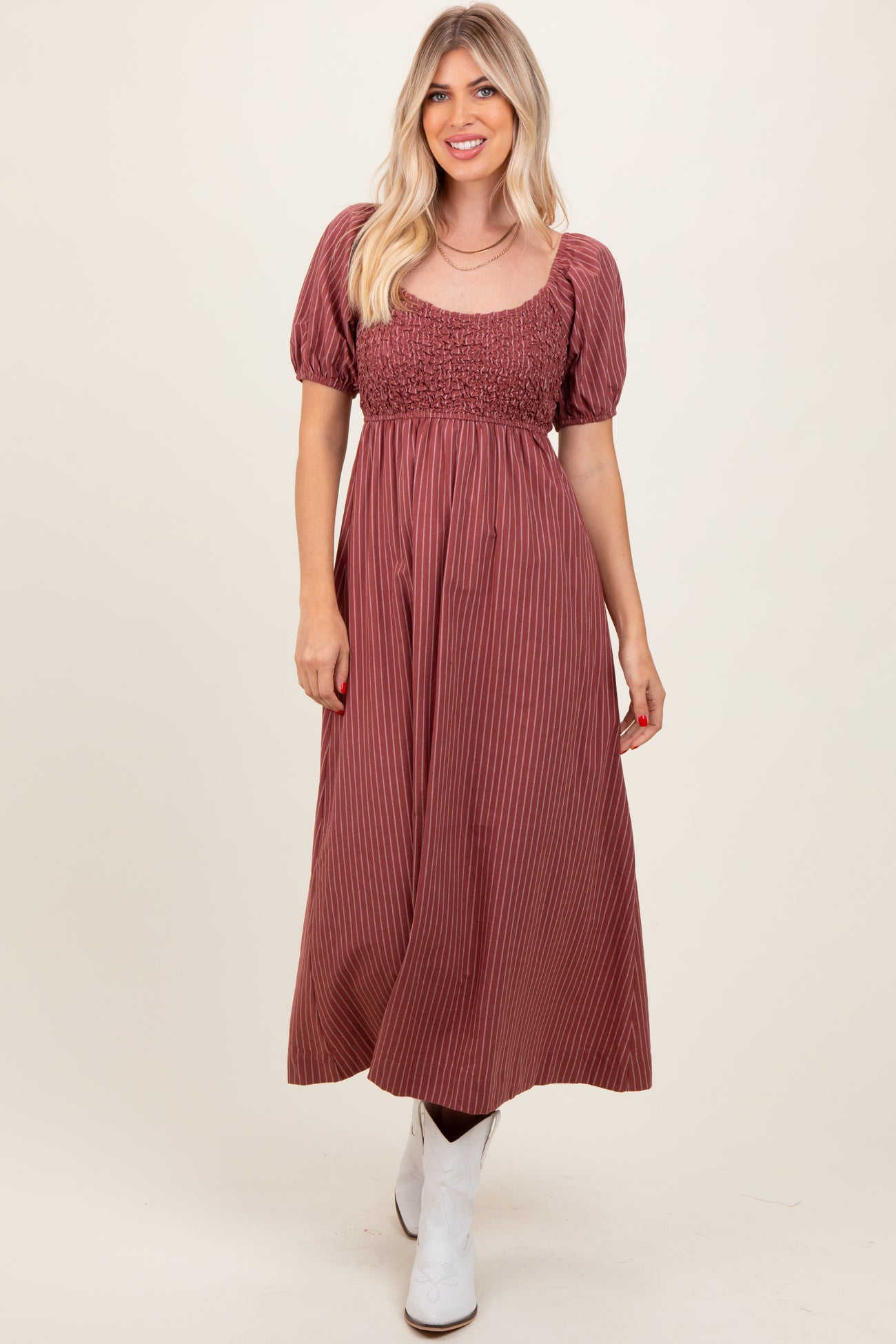woman wearing a burgundy striped maxi dress with a smocked bodice and puff sleeves, paired with white ankle boots