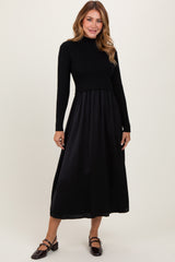 woman wearing a black long sleeve ribbed top and a flowy black midi dress with a fitted waist