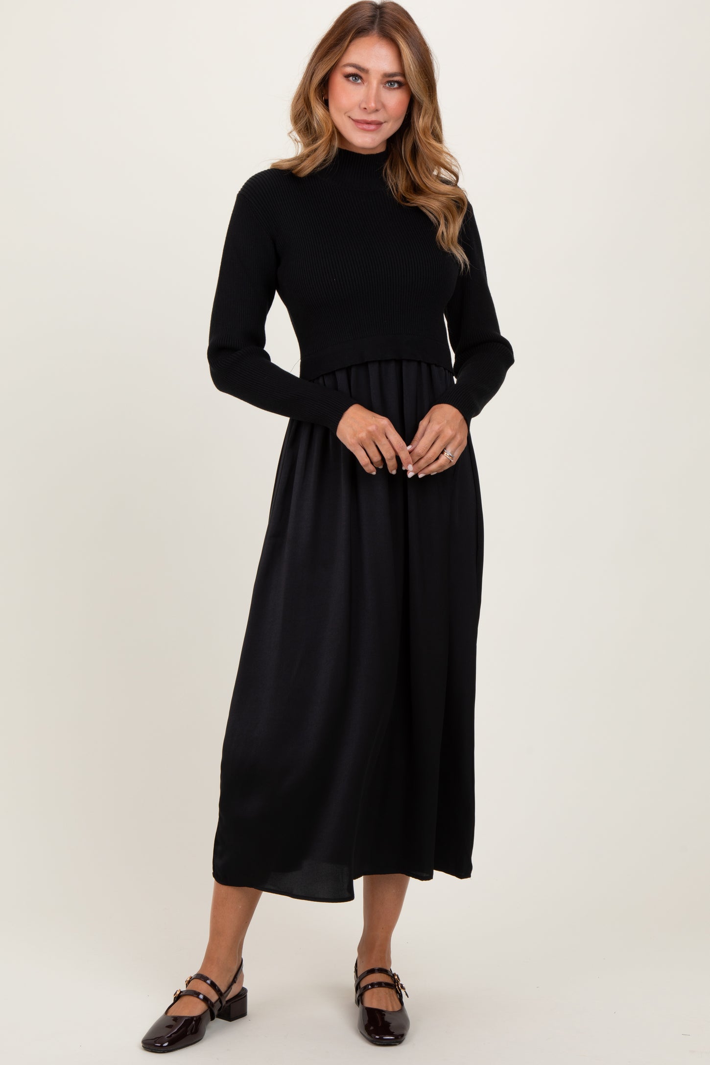 woman wearing a black knit long sleeve dress with a flowy satin skirt and flat shoes