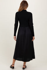 woman wearing a black ribbed long sleeve dress with a fitted bodice and flowing skirt, viewed from the back