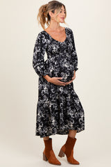 woman wearing a black floral maternity maxi dress with puff sleeves and holding her baby bump