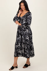 woman wearing a black and white floral maxi dress with a v-neckline and long sleeves, standing on a light background